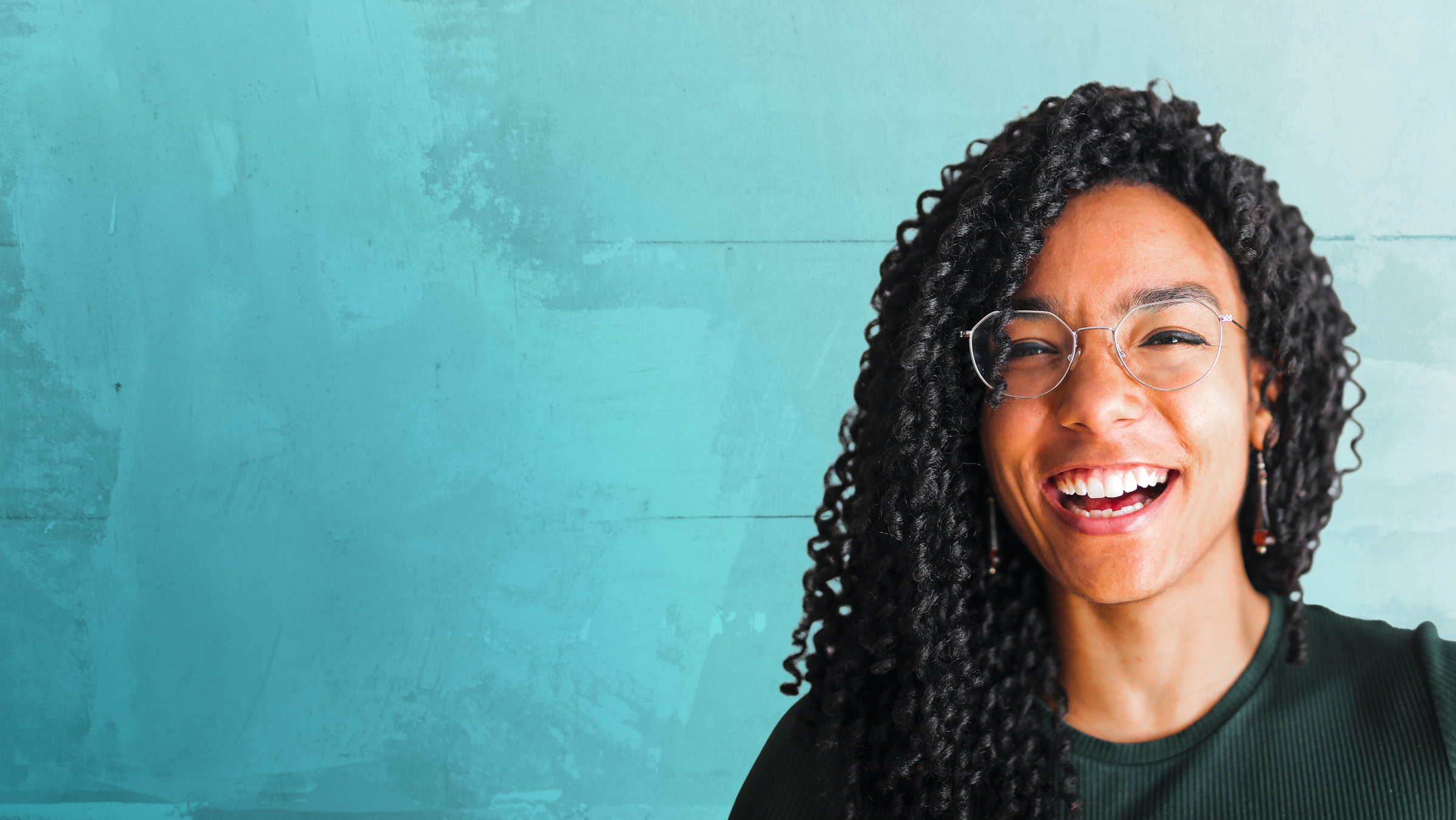 Woman with curly hair and glasses smiling against a teal background